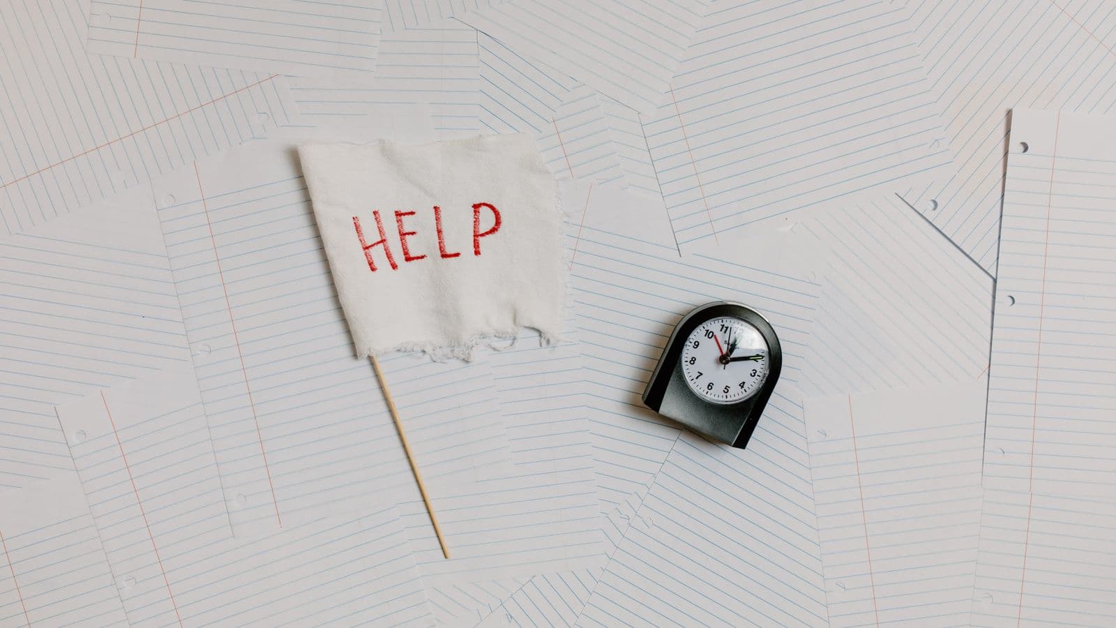Petit drapeau « help » et réveil posés sur des feuilles — créer son site soi-même en 24 heures